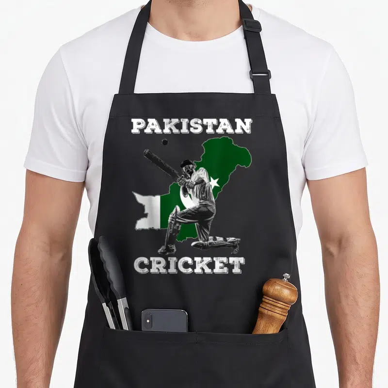 Pakistani cricket apron - Distressed PAKISTAN CRICKET text framing a batter in front of a green and white map silhouette — shown on a black cotton canvas apron against a white background