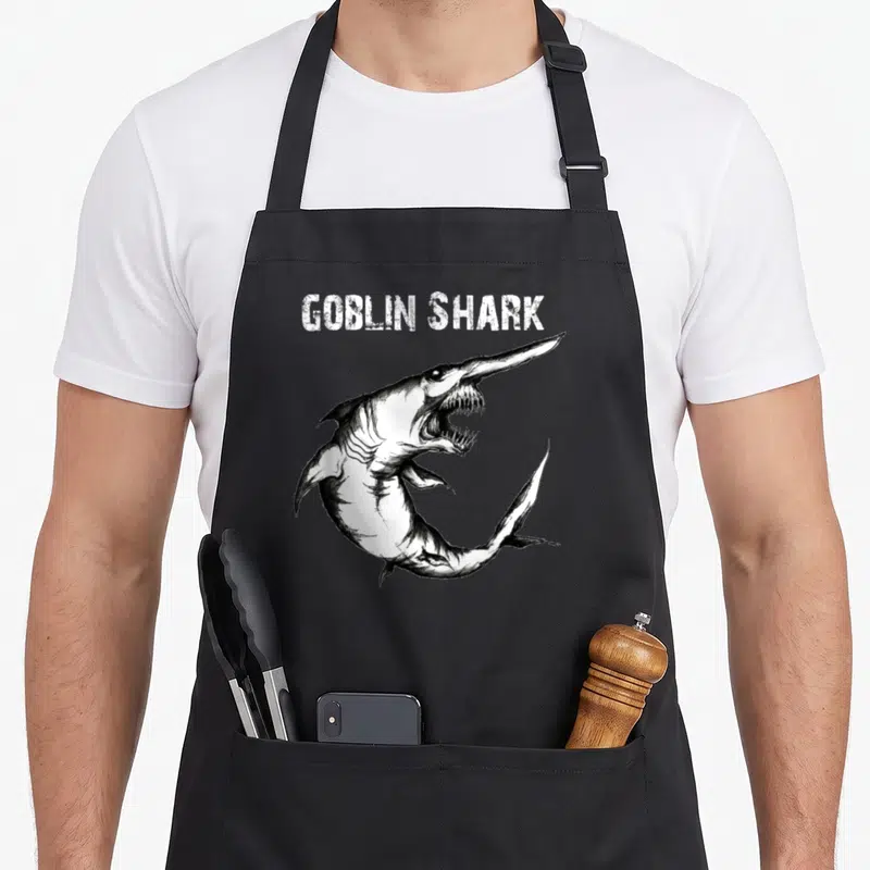 Funny goblin shark apron - White GOBLIN SHARK text above black line-art drawing of a shark with extended jaw — shown on a black cotton canvas apron against a white background