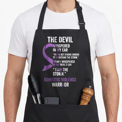 Devil domestic aprons - Purple awareness ribbon overlapping white and purple text reading Devil Whispered In My Ear — shown on a black cotton canvas apron against a white background