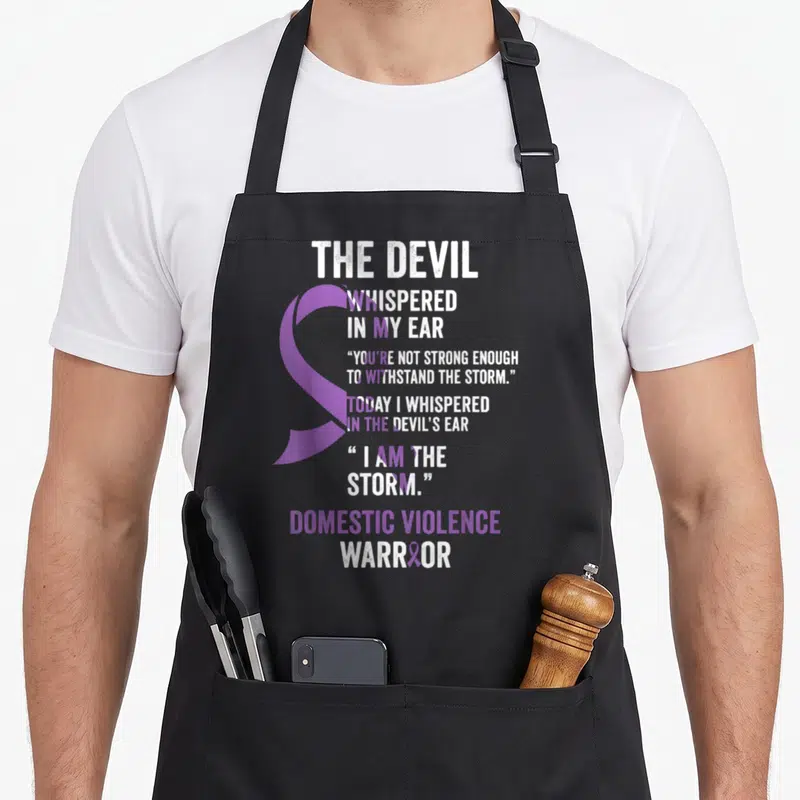 Devil domestic aprons - Purple awareness ribbon overlapping white and purple text reading Devil Whispered In My Ear — shown on a black cotton canvas apron against a white background