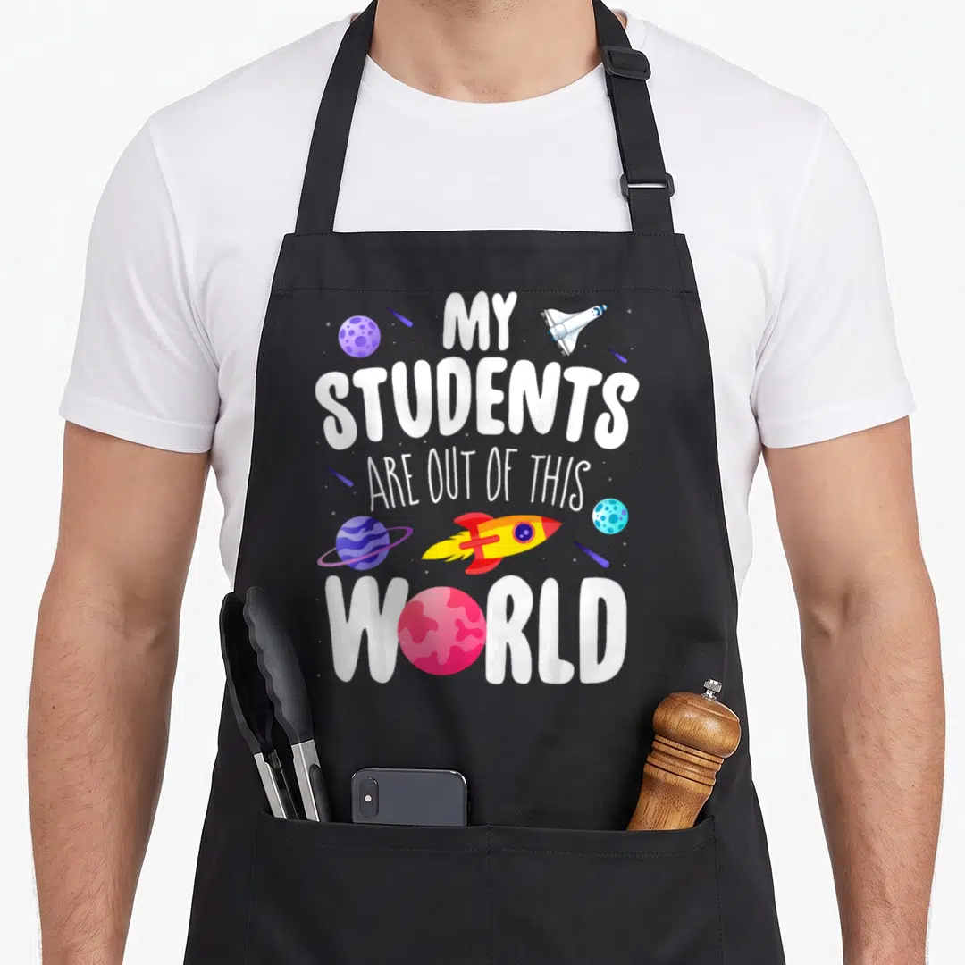 Student space teacher apron - My Students Are Out Of This World text with cartoon planets and rockets in purple blue — shown on a black cotton canvas apron against a white background