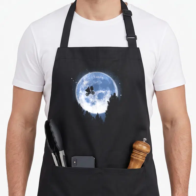 Elliot bicycle apron - Large blue moon with bicycle silhouette and grey trees — shown on a black cotton canvas apron against a white background
