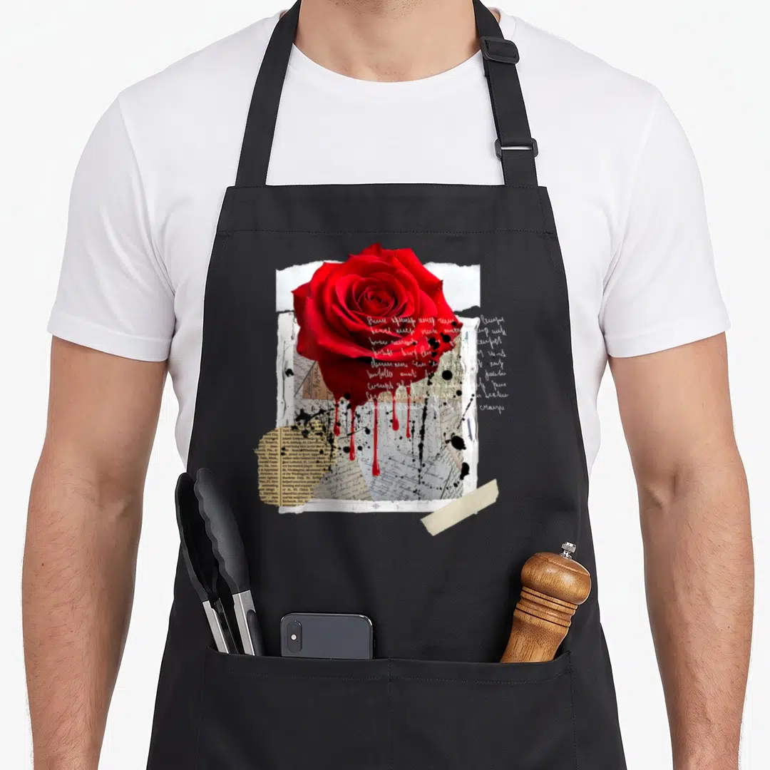 Dark streetwear apron - Red rose over torn papers, black ink splatters, and beige tape collage — shown on a black cotton canvas apron against a white background