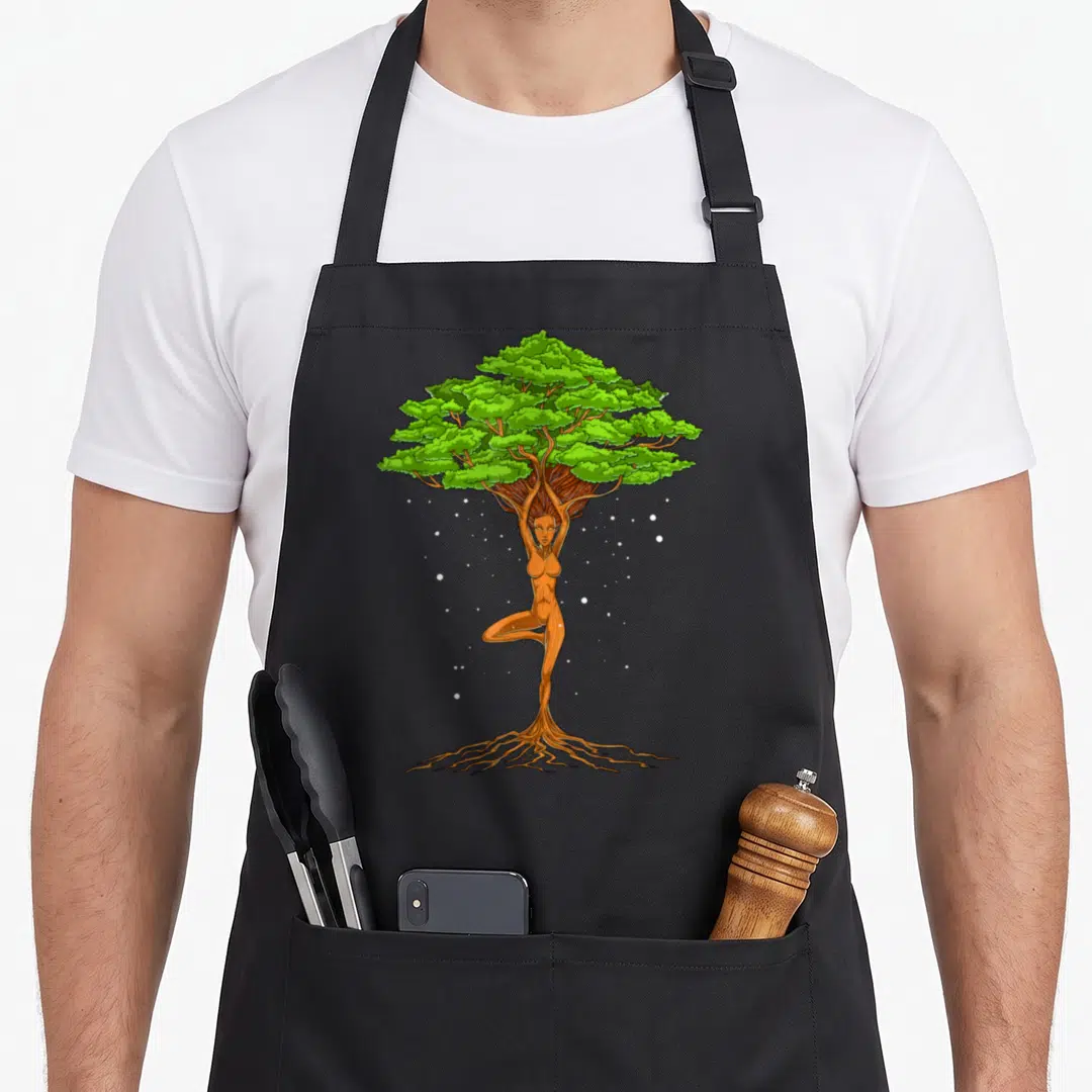 Yoga spiritual tree apron - Tree woman merging with trunk, green leaves, brown roots, white dots, cartoon style — shown on a black cotton canvas apron against a white background