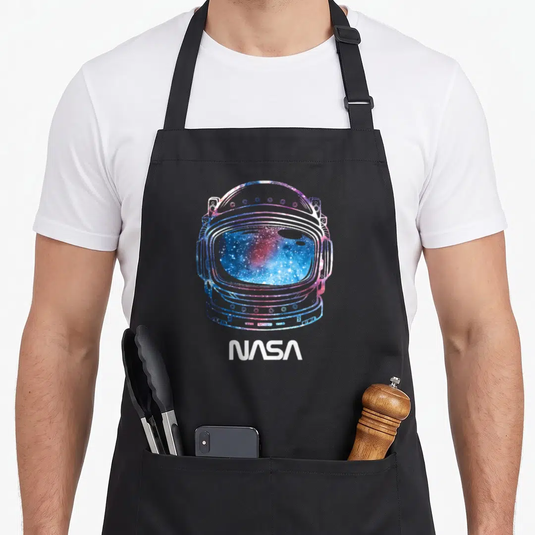 Galaxy nasa apron - Minimalist astronaut helmet outline filled with blue purple pink galaxy texture above white NASA — shown on a black cotton canvas apron against a white background