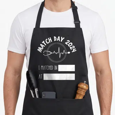 Match doctor apron - White Match Day 2024 text stethoscope EKG line and two fill-in boxes — shown on a black cotton canvas apron against a white background