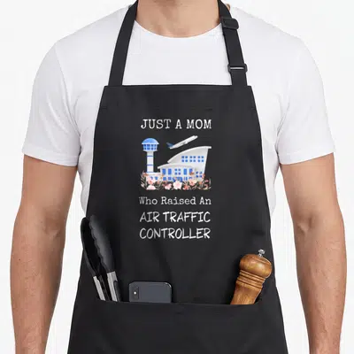 Raised air mom apron - Airport terminal and tower illustration with pink flowers and text Just A Mom Who Raised An Air — shown on a black cotton canvas apron against a white background