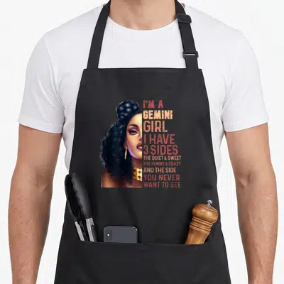 Gemini astrology zodiac aprons - Realistic woman portrait next to stacked red and gold text listing three personality — shown on a black cotton canvas apron against a white background