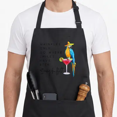 Wrinkle mexican apron - Cartoon parrot in sombrero on cocktail glass beside stacked text quote — shown on a black cotton canvas apron against a white background