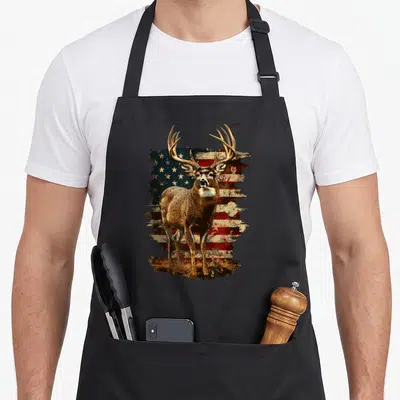 Deer 4th of july apron - Brown deer standing in front of distressed red white and blue American flag with grass at feet — shown on a black cotton canvas apron against a white background
