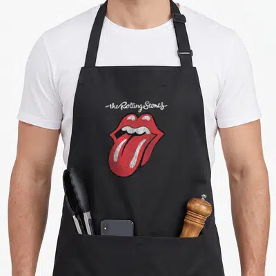 Cute script rolling stones apron - White script text above a distressed red lips and tongue graphic outlined in black — shown on a black cotton canvas apron against a white background