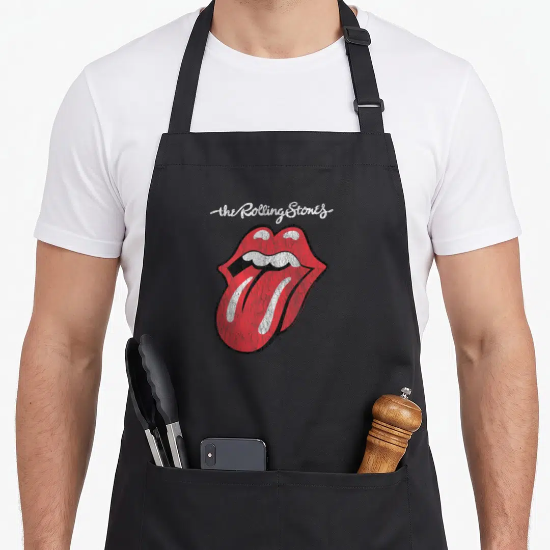 Cute script rolling stones apron - White script text above a distressed red lips and tongue graphic outlined in black — shown on a black cotton canvas apron against a white background