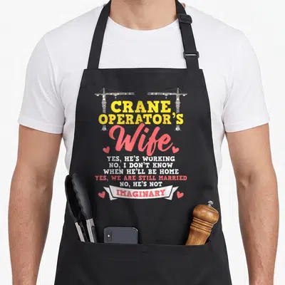 Crane construction worker apron - Crane Operator's Wife text with two cranes and four pink hearts — shown on a black cotton canvas apron against a white background
