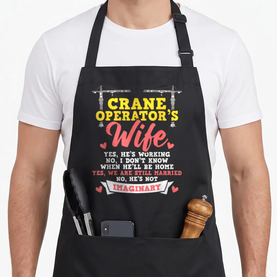 Crane construction worker apron - Crane Operator's Wife text with two cranes and four pink hearts — shown on a black cotton canvas apron against a white background
