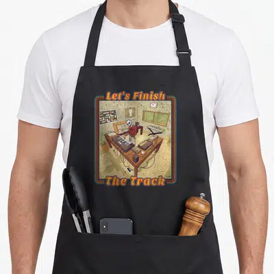 Electronic synthesizer apron - Skeleton in studio with modular synth and text Let's Finish The Track — shown on a black cotton canvas apron against a white background