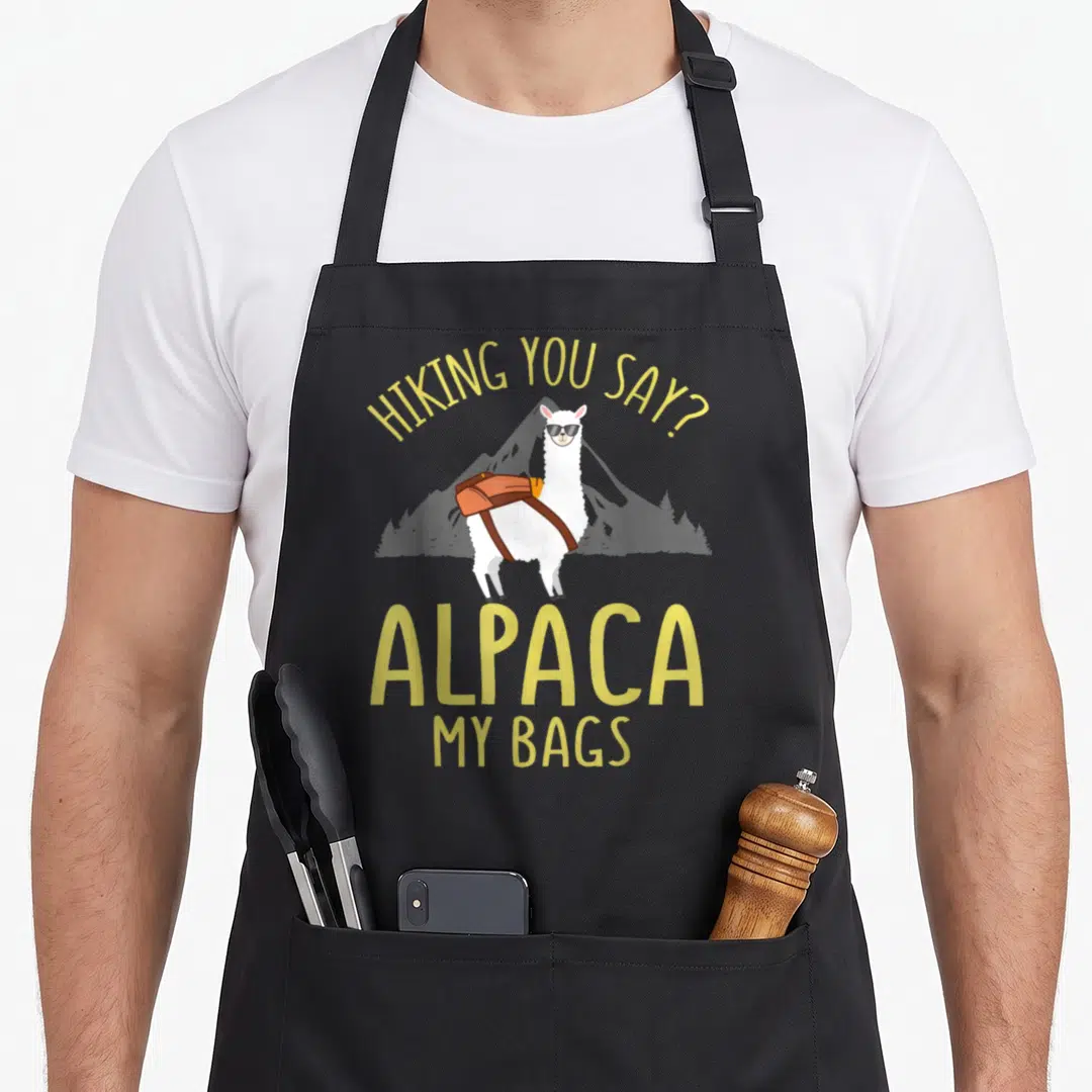 Father alpaca apron - Cartoon alpaca with orange backpack and sunglasses under yellow hiking pun text — shown on a black cotton canvas apron against a white background