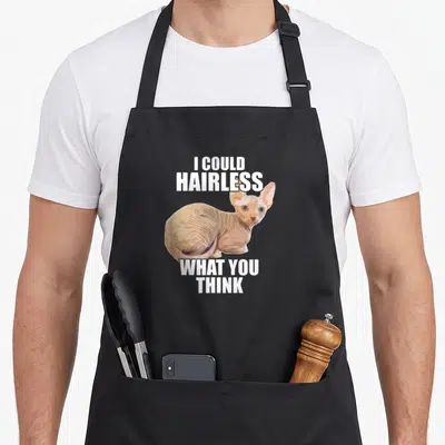 Hairless cat apron - Cartoon beige hairless cat between white text I Could Hairless What You Think — shown on a black cotton canvas apron against a white background