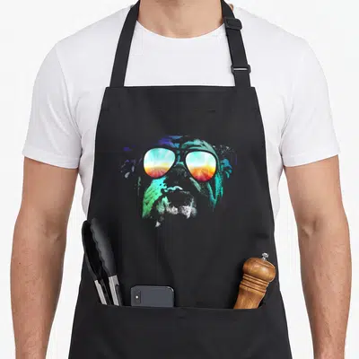 Disco english chef aprons - Cartoon dog head with sunglasses reflecting a sunset in blue, green, red, and yellow — shown on a black cotton canvas apron against a white background