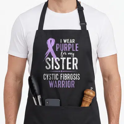 Sister cystic fibrosis awareness apron - Purple ribbon and I WEAR PURPLE for my SISTER CYSTIC FIBROSIS WARRIOR text — shown on a black cotton canvas apron against a white background