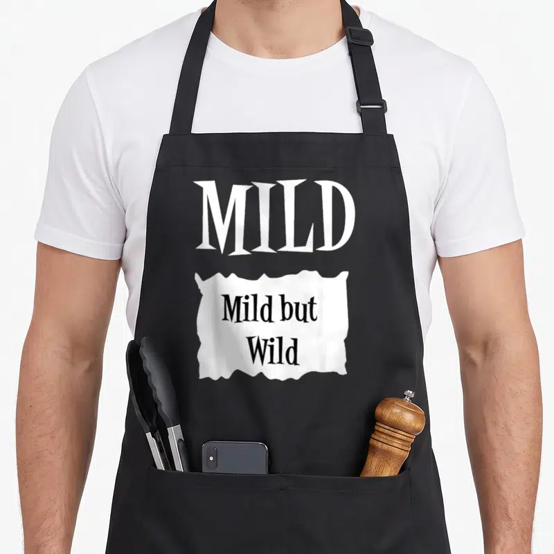 Mild halloween apron - White MILD text above torn paper reading Mild but Wild in black — shown on a black cotton canvas apron against a white background