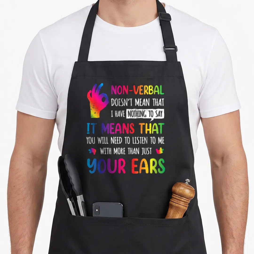 Nonverbal hand quotes apron - Rainbow hand making OK sign beside stacked text about nonverbal communication and autism — shown on a black cotton canvas apron against a white background