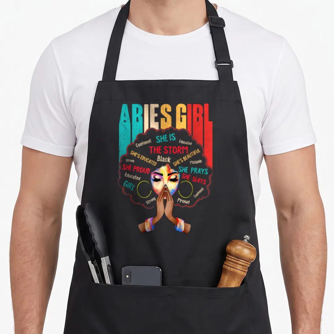 She aries kitchen apron - ARIES GIRL text above woman with praying hands inside red afro filled with affirming words — shown on a black cotton canvas apron against a white background