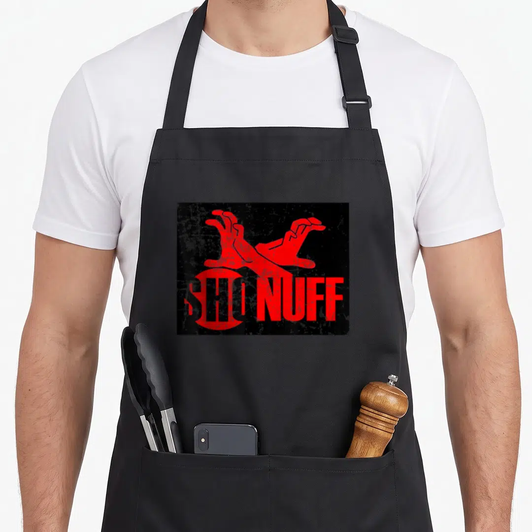 Sho distressed apron - Two red hands above red ENOUGH NUFF text on distressed black rectangle — shown on a black cotton canvas apron against a white background