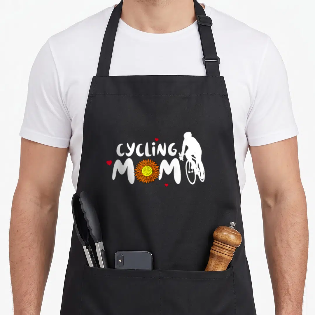 Funny cycling apron - CYCLING MOM text with sunflower O and white cyclist silhouette in orange red white — shown on a black cotton canvas apron against a white background