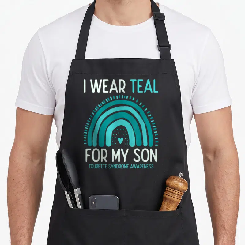 Son tourette awareness apron - Teal rainbow with small heart and text I WEAR TEAL FOR MY SON TOURETTE SYNDROME AWARENESS — shown on a black cotton canvas apron against a white background