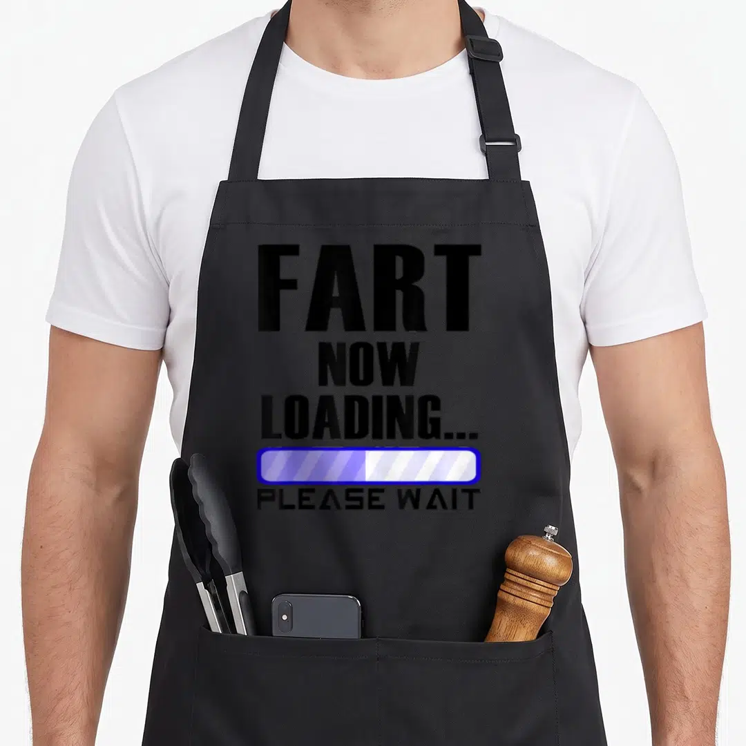 Fart dad joke apron - Black text FART NOW LOADING PLEASE WAIT with blue and white loading bar graphic — shown on a black cotton canvas apron against a white background
