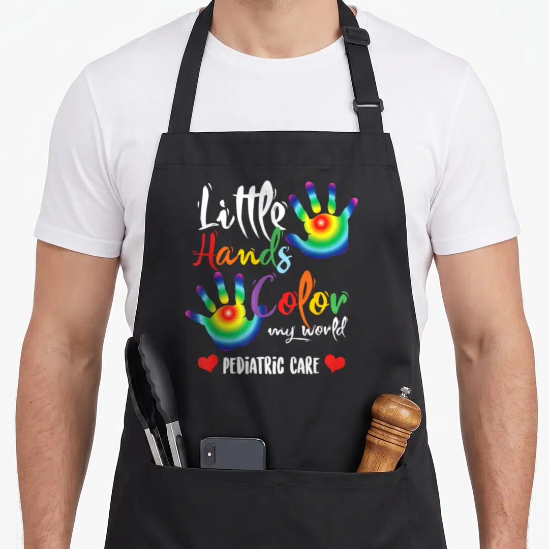 Pediatric nurse apron - Rainbow handprints surrounding Little Hands Color my world PEDIATRIC CARE text with red hearts — shown on a black cotton canvas apron against a white background
