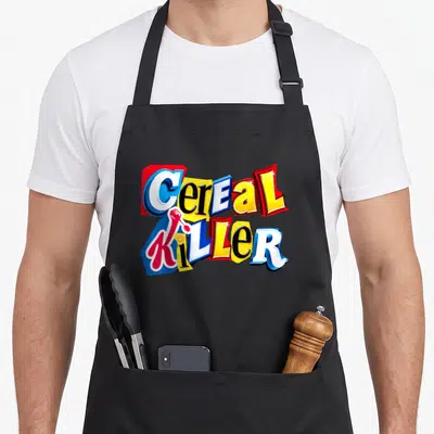 Cereal family aprons - Cereal KILLER text with red spoon and yellow loop in red blue yellow white — shown on a black cotton canvas apron against a white background