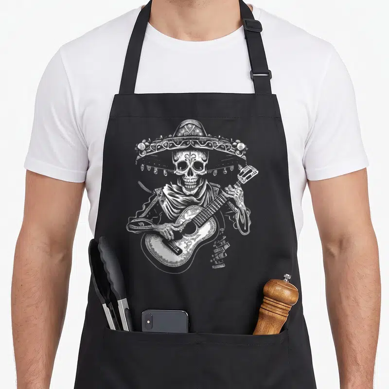 Guitar day of the dead apron - White line-art skeleton in sombrero and poncho playing a guitar — shown on a black cotton canvas apron against a white background