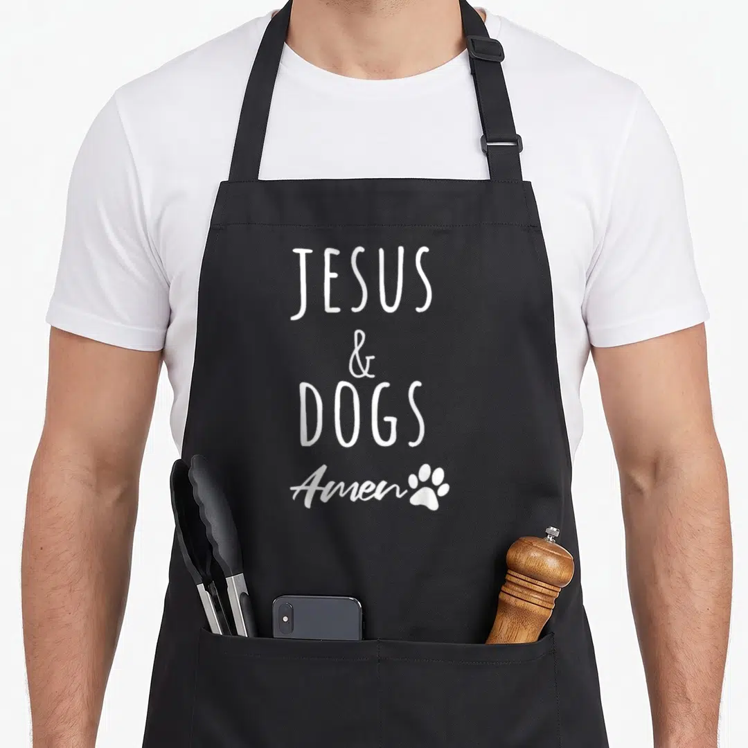 Christ dog apron - White stacked text JESUS & DOGS Amen with a small paw print on a black background — shown on a black cotton canvas apron against a white background