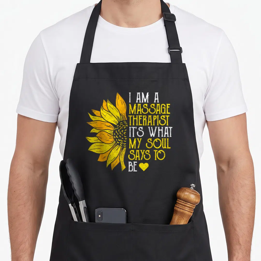 Sunflower massage therapist apron - Yellow sunflower graphic beside white and yellow stacked text ending with a small — shown on a black cotton canvas apron against a white background