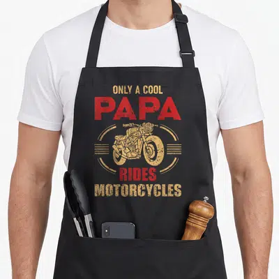 Ride father day apron - Red and gold retro motorcycle graphic with stacked text reading only a cool papa rides — shown on a black cotton canvas apron against a white background