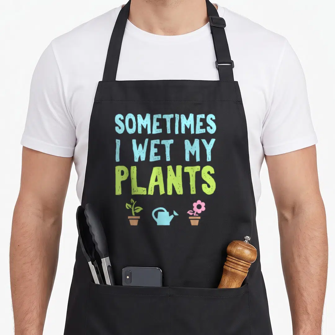Wet plant apron - Stacked text SOMETIMES I WET MY PLANTS above cartoon potted plants and blue watering can — shown on a black cotton canvas apron against a white background