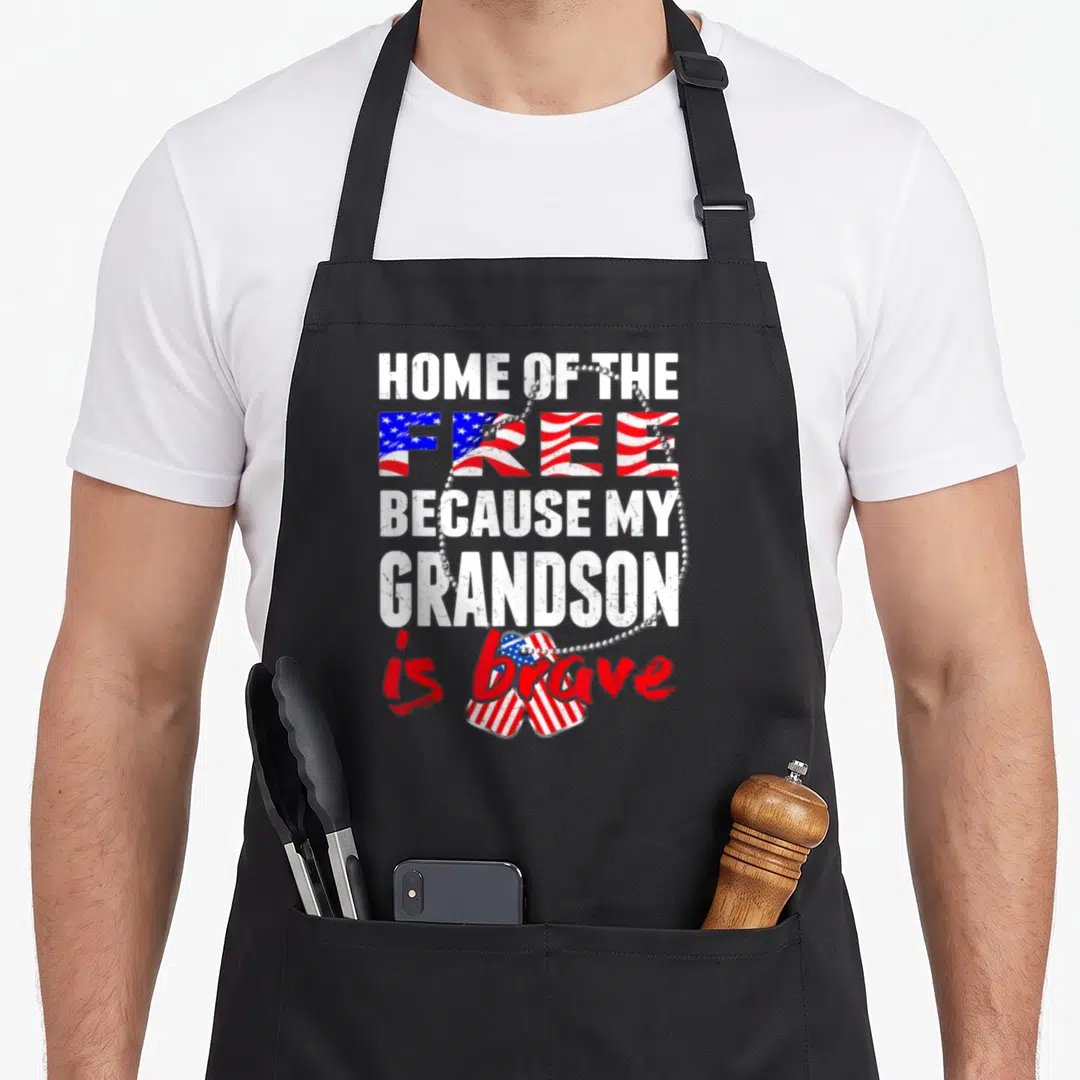 Grandson veterans apron - Stacked text reading Home of the Free Because My Grandson is brave above two flag-filled dog — shown on a black cotton canvas apron against a white background