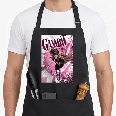 Card x apron - GAMBIT text above leaping character with staff and flying cards in pink and purple — shown on a black cotton canvas apron against a white background