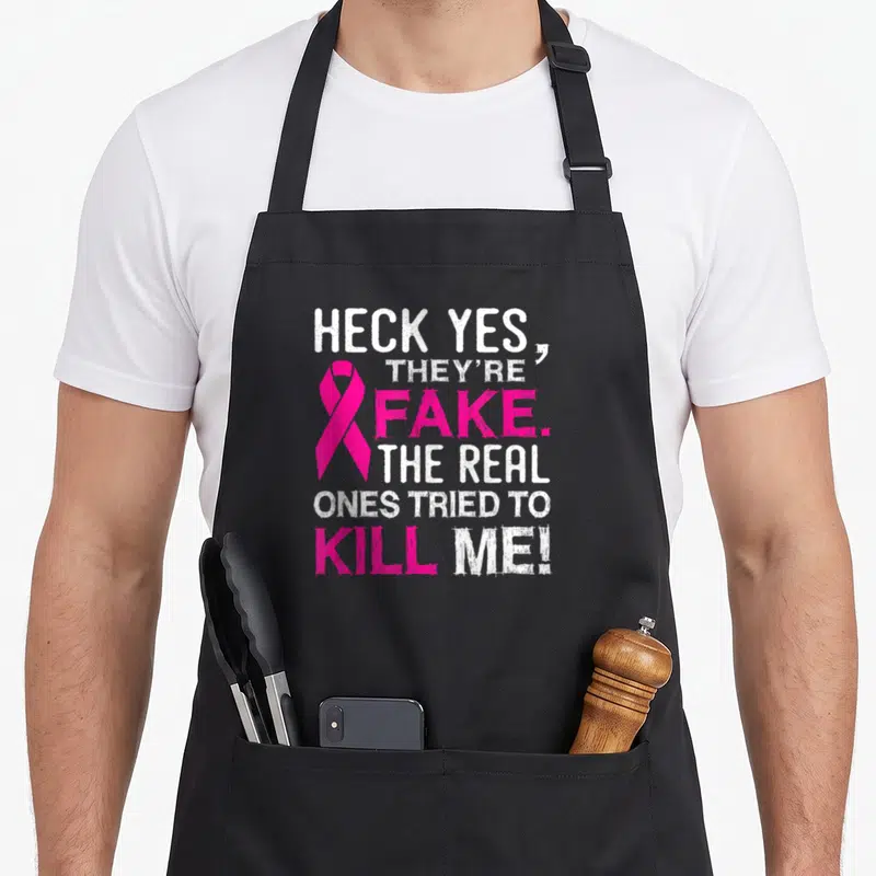 Fake all these apron - HECK YES THEYRE FAKE text with pink ribbon and distressed typography — shown on a black cotton canvas apron against a white background