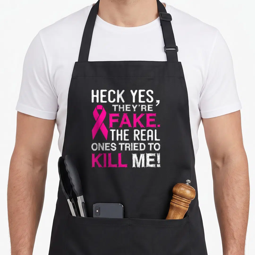Fake all these apron - HECK YES THEYRE FAKE text with pink ribbon and distressed typography — shown on a black cotton canvas apron against a white background