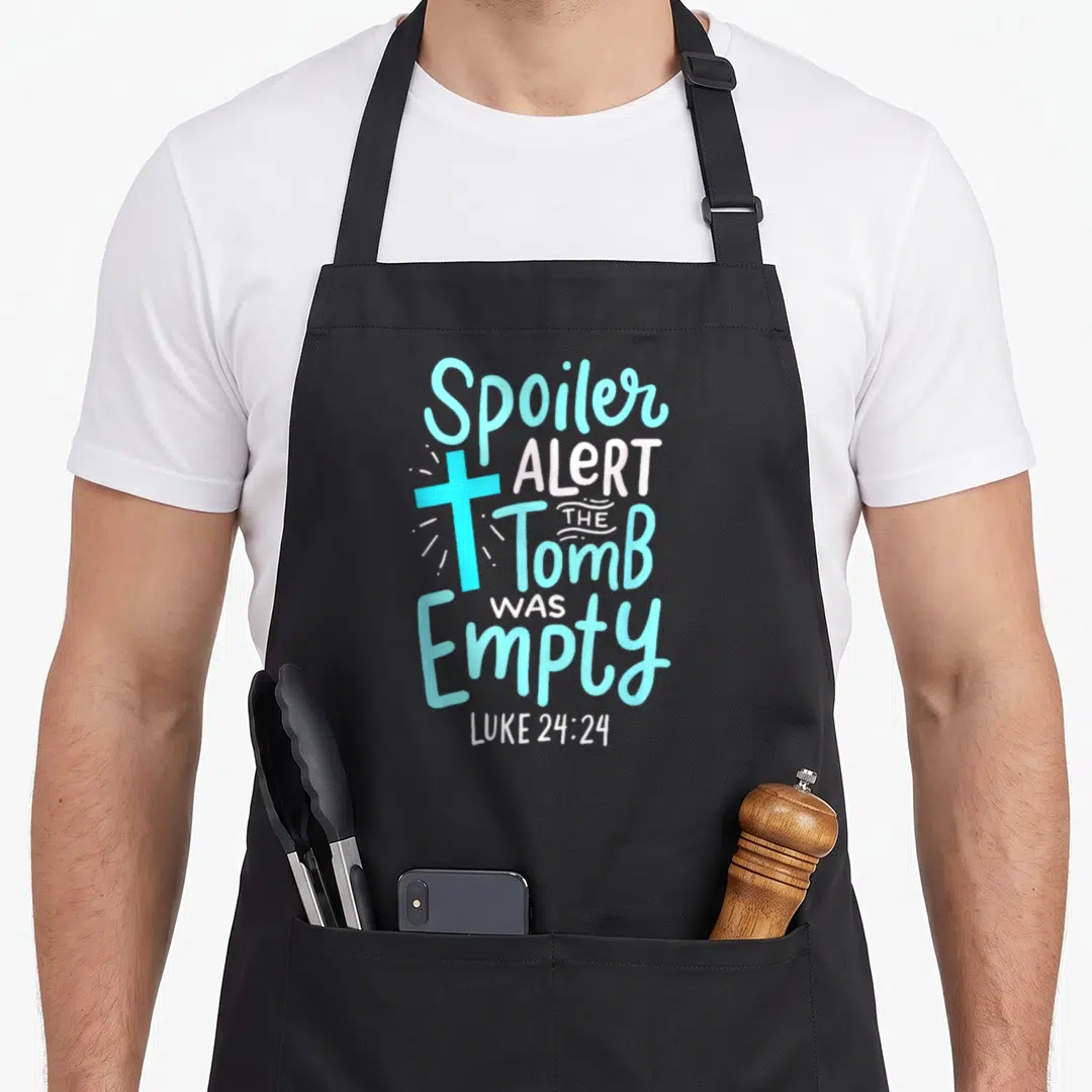 Alert easter apron - Vertical text Spoiler Alert The Tomb Was Empty Luke 24:24 with light blue cross and white rays — shown on a black cotton canvas apron against a white background