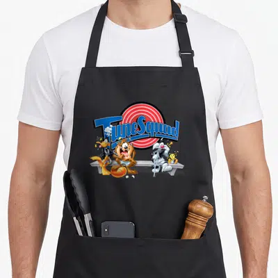Space k squad apron - TuneSquad text over red circle with four cartoon characters on a bench and an orange basketball — shown on a black cotton canvas apron against a white background