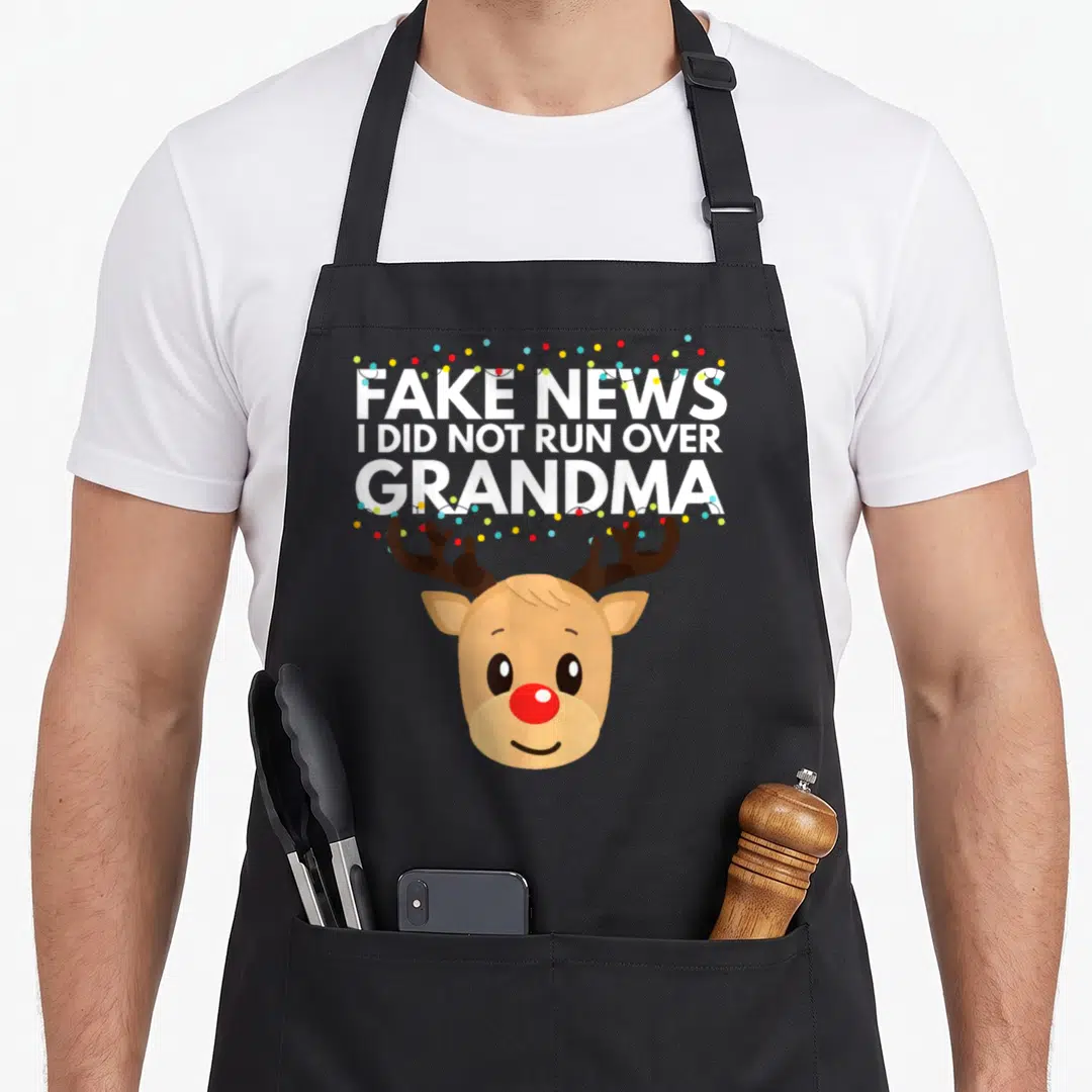 Casual holiday christmas aprons - Cartoon reindeer head with white text FAKE NEWS I DID NOT RUN OVER GRANDMA — shown on a black cotton canvas apron against a white background