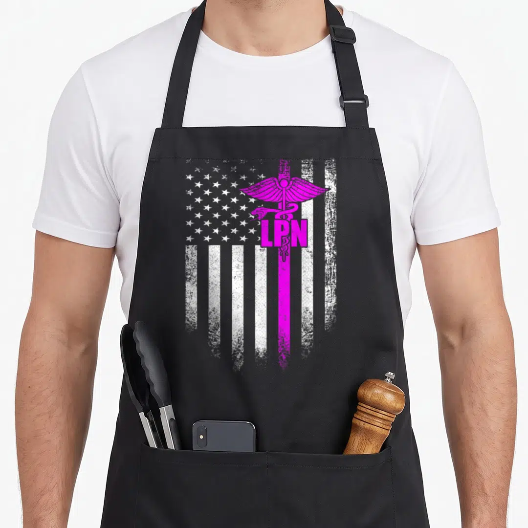 Lpn american flag apron - Magenta caduceus with LPN text over distressed grey and white American flag — shown on a black cotton canvas apron against a white background