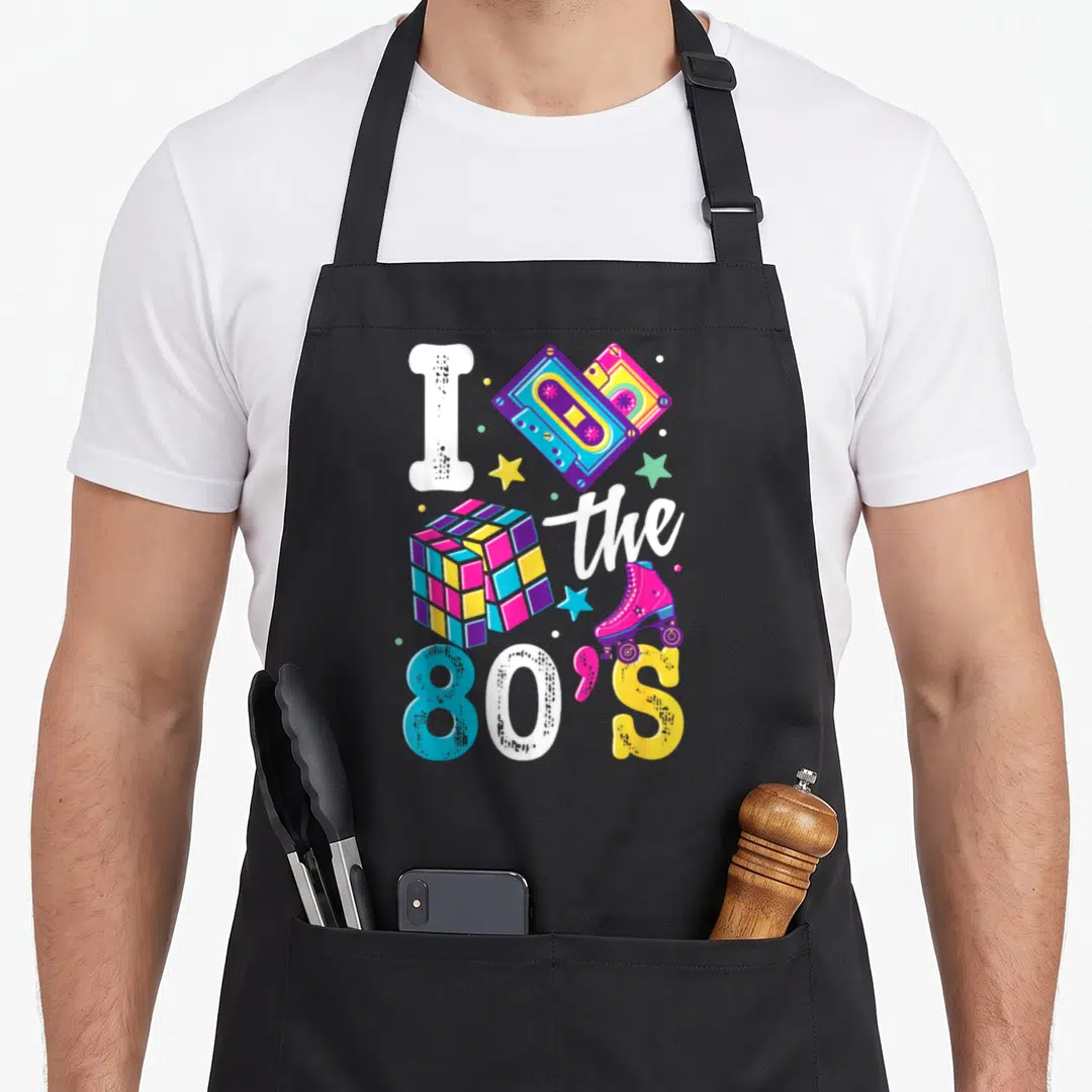 Supply 80s apron - I the 80'S graphic with cassette, cube, skate, and stars in pink blue yellow purple white — shown on a black cotton canvas apron against a white background