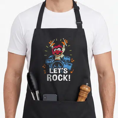 Drum animal apron - Monster drummer behind blue drums with raised sticks and white LET'S ROCK text surrounded by orange — shown on a black cotton canvas apron against a white background