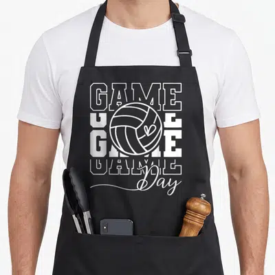Volley game aprons - White block letters GAME and script Day surrounding a volleyball outline — shown on a black cotton canvas apron against a white background