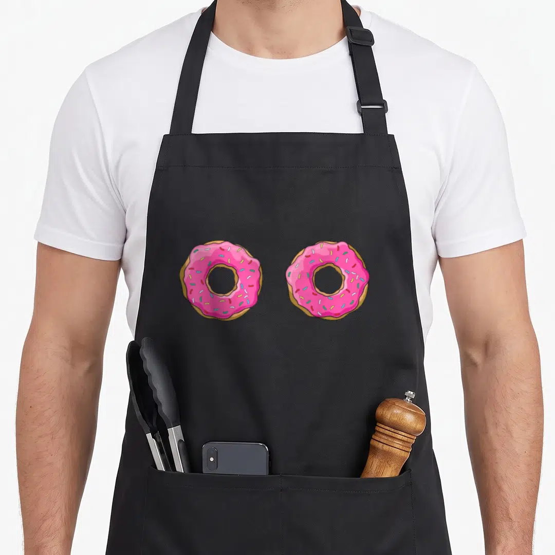 Doughnut donut apron - Two pink frosted donuts with sprinkles in a cartoon style side by side — shown on a black cotton canvas apron against a white background