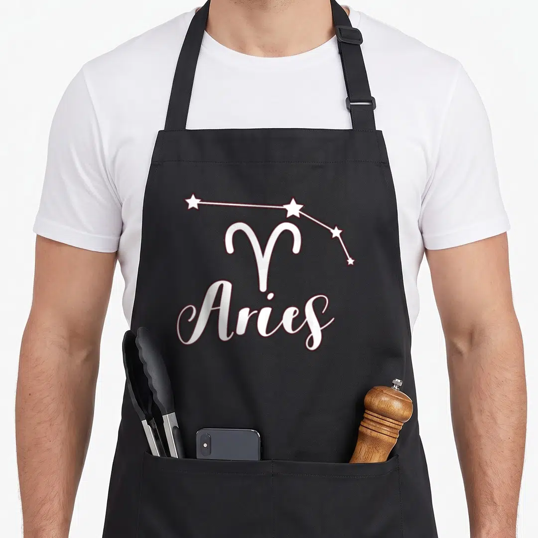 Zodiac sign aries kitchen apron - White Aries symbol and constellation with cursive text outlined in maroon — shown on a black cotton canvas apron against a white background